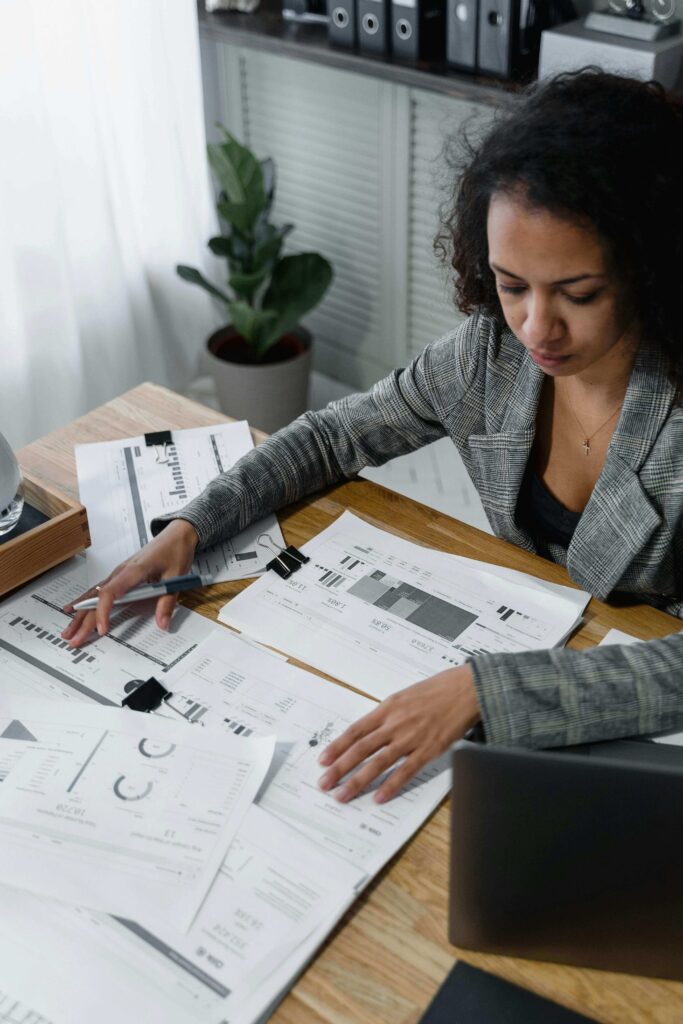 A woman sitting at a desk reviewing her credit report documents with a laptop and notebook, focused and determined.
